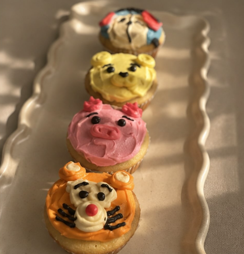 Four hand-decorated animal character cupcakes on a scalloped tray